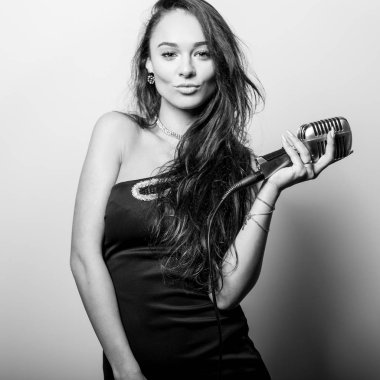 Mikrofon ile siyah elbiseli genç şehvetli kadın. Siyah-beyaz portre.