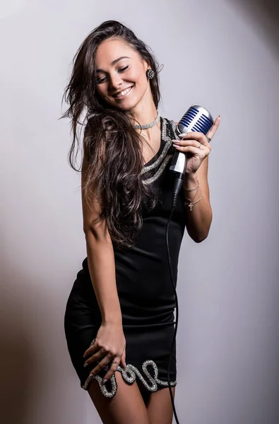Junge sinnliche Frau im schwarzen Kleid mit Mikrofon. — Stockfoto