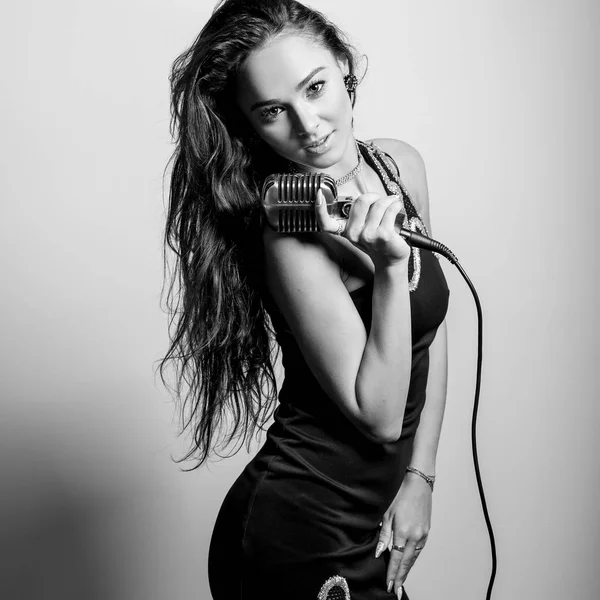 Sensuele jongedame in zwarte jurk met microfoon. Zwart-wit portret. — Stockfoto