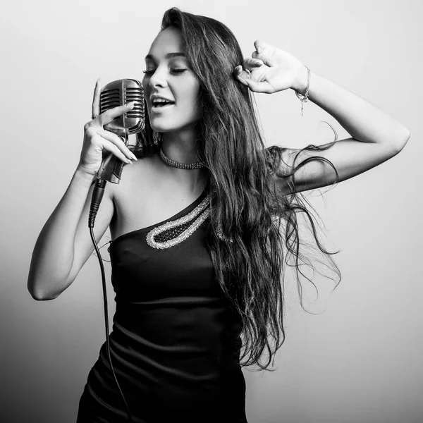 Young sensual woman in black dress with microphone. Black-white portrait. — Stock Photo, Image