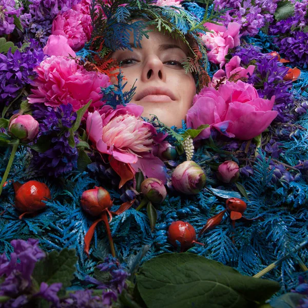 Vrouwelijk portret in sprookjesachtige stylization omgeven met natuurlijke bloemen. — Stockfoto