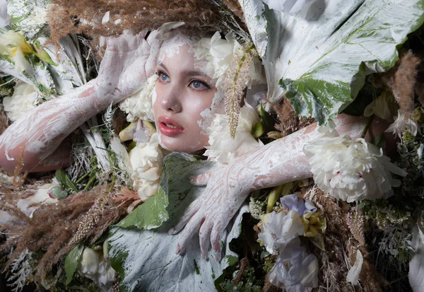 Ženský portrét v pohádkovém stylu obklopený přírodními rostlinami a květinami. — Stock fotografie