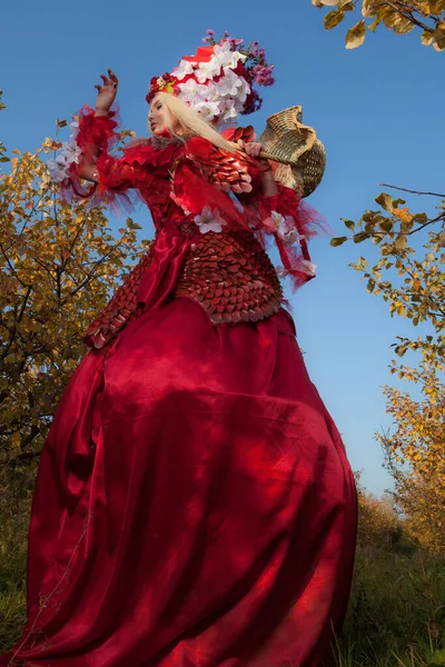 Zmysłowa blondynka dziewczyna w fantasy czerwony bajki stylizacji w jabłkowym parku. — Zdjęcie stockowe