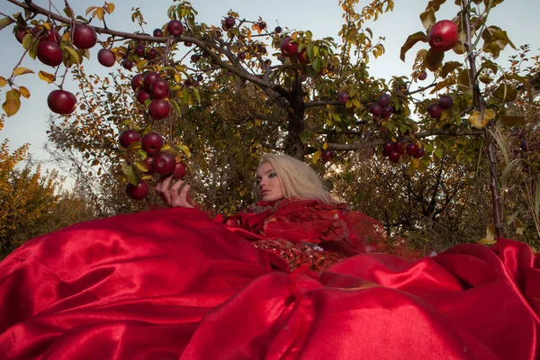 Zmysłowa blondynka dziewczyna w fantasy czerwony bajki stylizacji w jabłkowym parku. — Zdjęcie stockowe