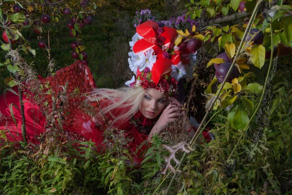 Sensual blond girl in fantasy red fairy tale stylization in apple park. — Stock Photo, Image