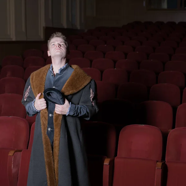 Actor dressed historical costume in interior of old theater.