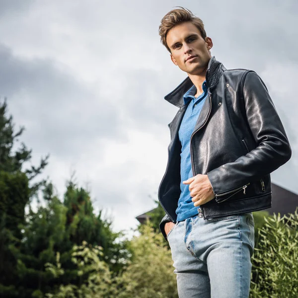 Joven hombre guapo en la clásica chaqueta de cuero posan en el jardín de verano . — Foto de Stock