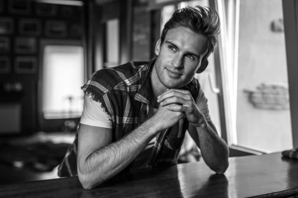 Beau jeune homme en vêtements décontractés pose contre l'intérieur de la maison. Portrait noir-blanc . — Photo