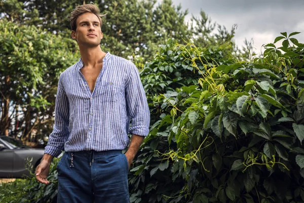 Νέος όμορφος άντρας σε casual ρούχα ποζάρει στον καλοκαιρινό κήπο. — Φωτογραφία Αρχείου