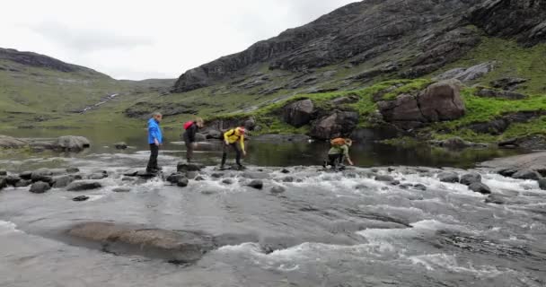 Skotsko, Velká Británie - 30. května 2019: Skupina cestovatelů přechází přes kameny v řece. — Stock video