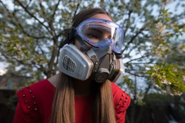 Korunma derecesinde maske takmış güzel bir kız portresi. Bahar bahçesinin alacakaranlık karanlığında poz veriyor..
