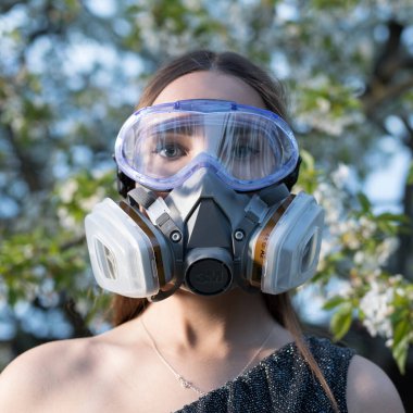 Korunma derecesinde maske takmış güzel bir kız portresi. Bahar bahçesinin alacakaranlık karanlığında poz veriyor..