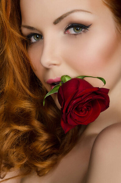 Woman with long red hair holds beautiful rose in her mouth