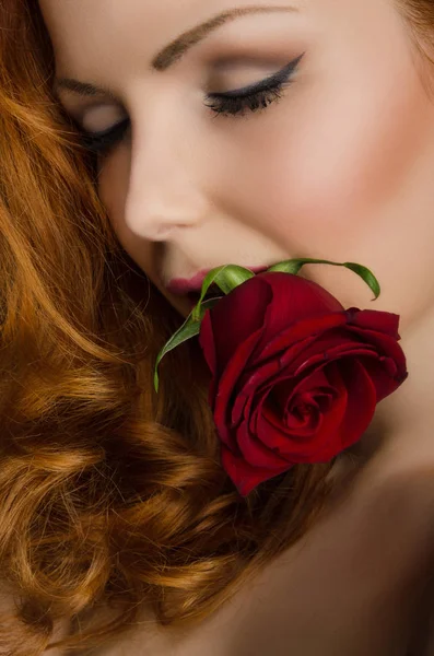 Young woman with curly red hair holds rose in her mouth — Stock Photo, Image