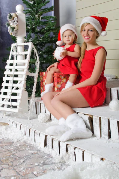 Mutlu anne ve Noel Baba'nın takım elbiseli kızı kar altında oturuyor — Stok fotoğraf