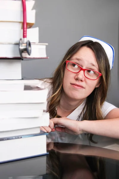 Enfermera joven con gorra mirando pila de libros Fotos de stock libres de derechos
