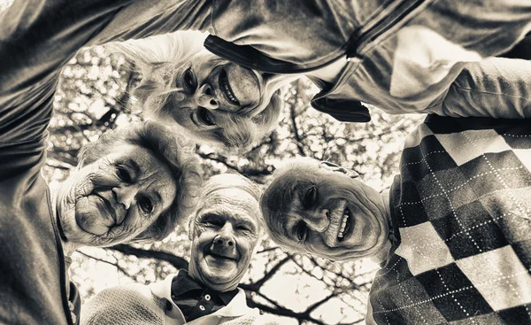 Four elder people looking down to camera relaxing happy outdoor — Stock Photo, Image