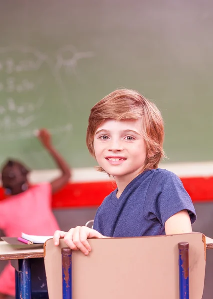 Rapaz sorridente na escola sentado em sala de aula — Fotografia de Stock