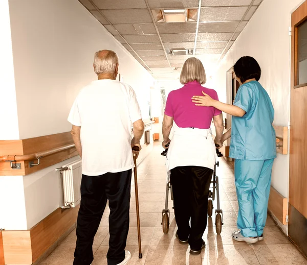 Instalação de reabilitação com dois pacientes mais velhos ajudados por enfermeira, costas vie — Fotografia de Stock