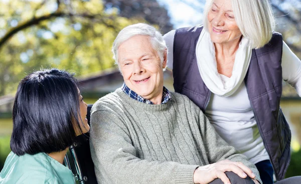 Elder couple in rehab clinic garden smiling with asian nurse — Stock Photo, Image