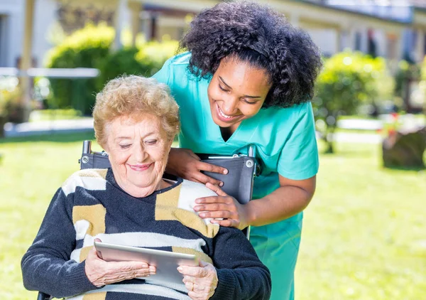 Tablet kullanımı için yaşlı kadın tekerlekli açıklayan hemşire — Stok fotoğraf
