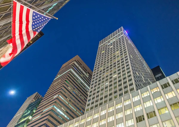 Размахивая флагом под высокими зданиями Манхэттена ночью, деловое сотрудничество — стоковое фото