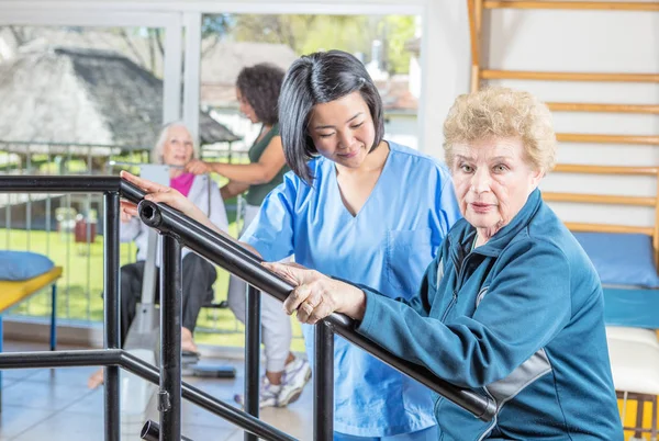 Спортивный зал реабилитационной клиники. Многорасовые медсестры помогают пожилым пациентам — стоковое фото