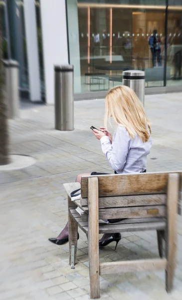 Деловая женщина пользуется мобильным телефоном на скамейке под открытым небом — стоковое фото