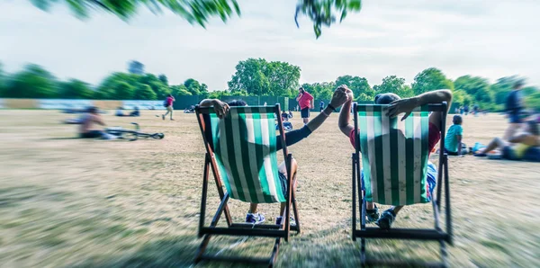 Pareja acostada en sillas de playa en un parque de la ciudad, vista trasera —  Fotos de Stock