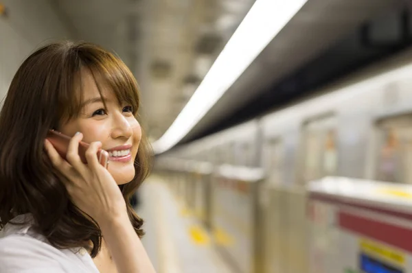 Asiatin entschuldigt sich am Telefon und wartet auf U-Bahn-Zug — Stockfoto