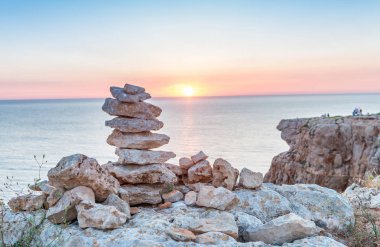 Stacked stones over the sea at sunset clipart