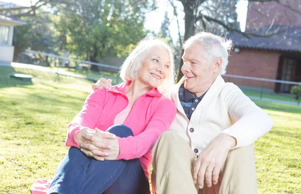 Ouderling paar glimlachend en ontspannen zitten in de tuin. — Stockfoto