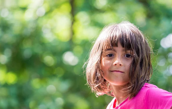 Schönes kleines Mädchen lächelt im Park und blickt in die Kamera — Stockfoto