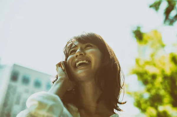 Счастливая азиатская деловая женщина на открытом воздухе выступая на мобильном телефоне — стоковое фото