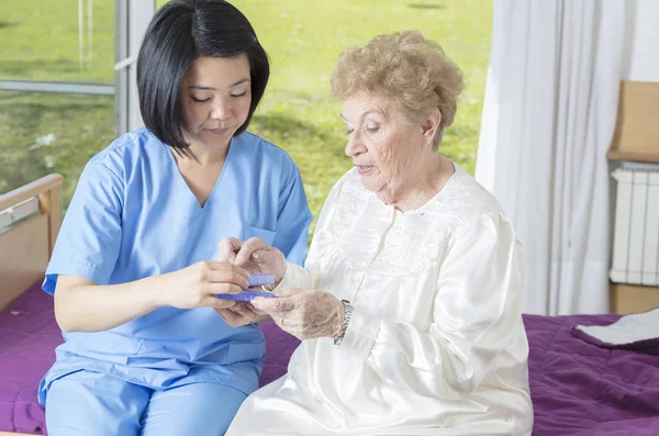 Ältere Frau im Krankenhaus nimmt Tablette von asiatischer Krankenschwester — Stockfoto