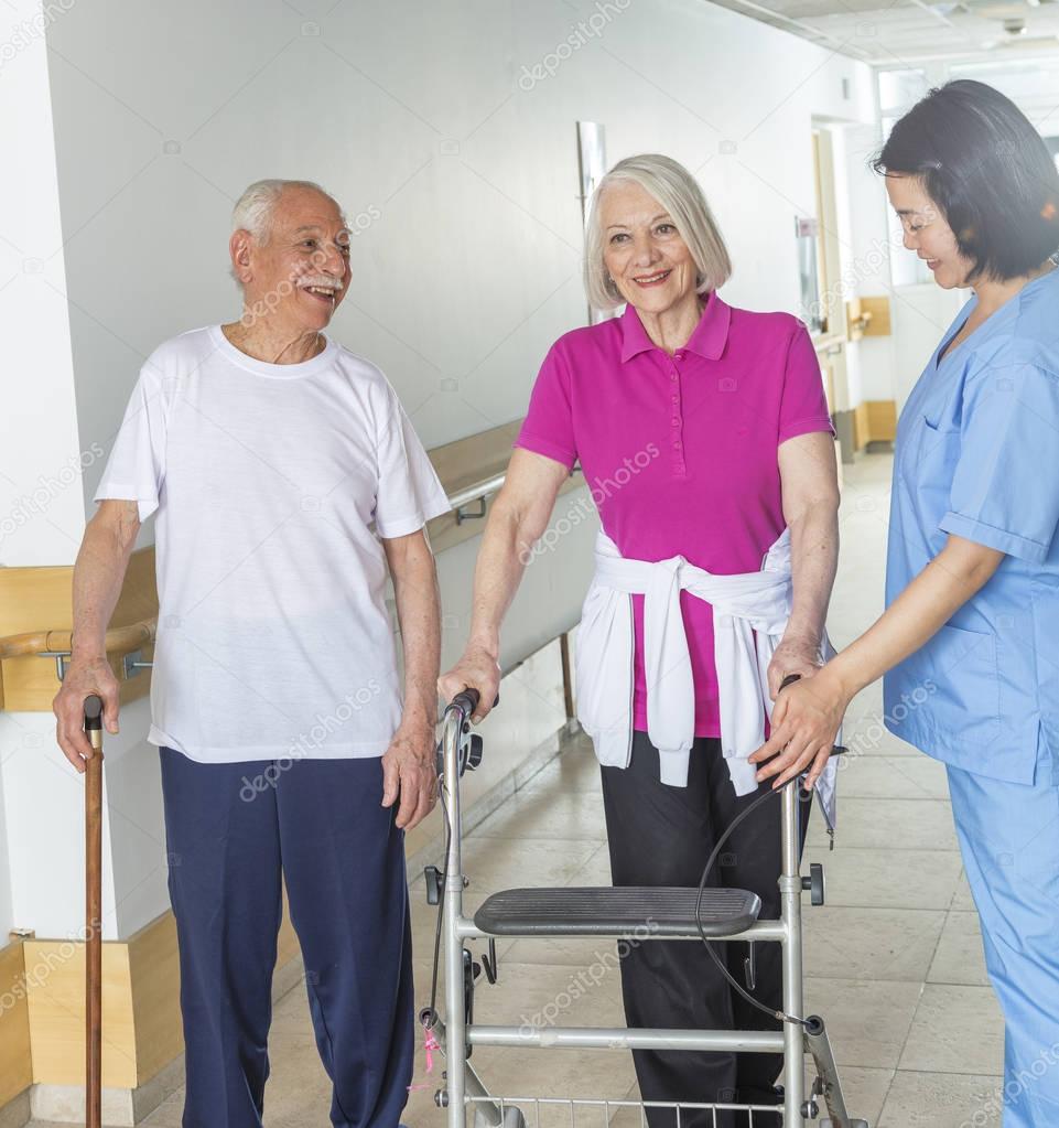Happy elderly couple of seniors in rehab clinic helped by asian 