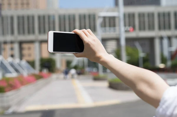 Braccio femminile con cellulare scattare foto di città — Foto Stock