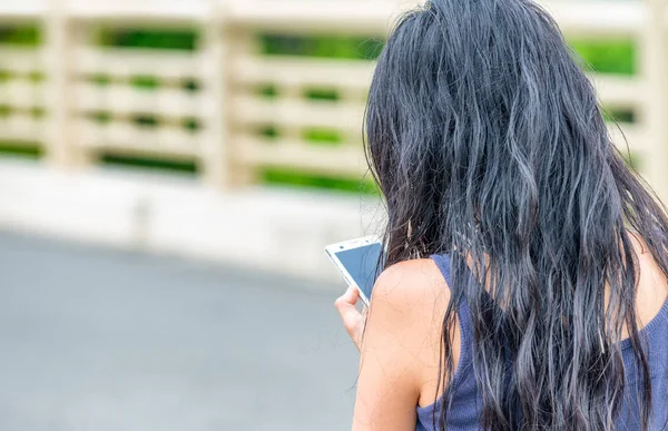 Девушка-брюнетка, пользующаяся смартфоном на улице, спина к спине — стоковое фото