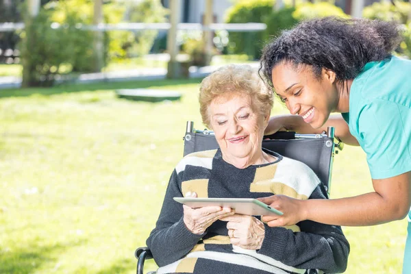 Mujer anciana usando tableta en el jardín ayudado por la enfermera —  Fotos de Stock