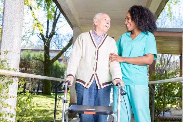 Active elderly retired man outdoor with african nurse — Stock Photo, Image