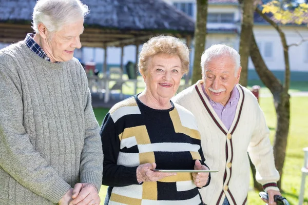 Three active elderly people outdoor reading tablet — Stock Photo, Image