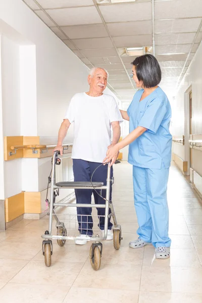 Медсестра допомагає літньому чоловікові з ходунками в лікарні — стокове фото