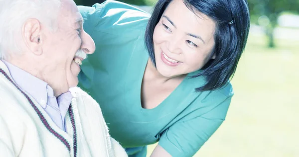 Idoso ativo aposentado homem ao ar livre com asiático enfermeira — Fotografia de Stock