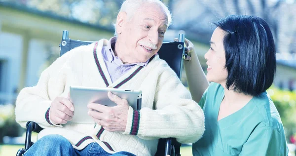 Actieve ouderen gepensioneerde man buiten lezing tablet met Aziatische nur — Stockfoto