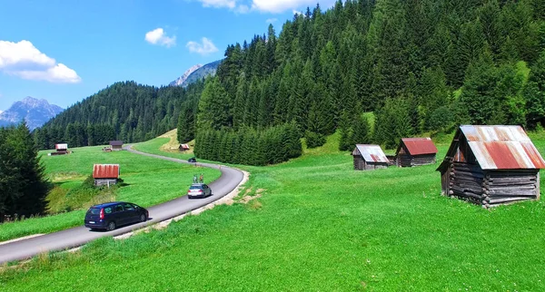 Aerial view of mountain road across meadows in summer season — Stock Photo, Image