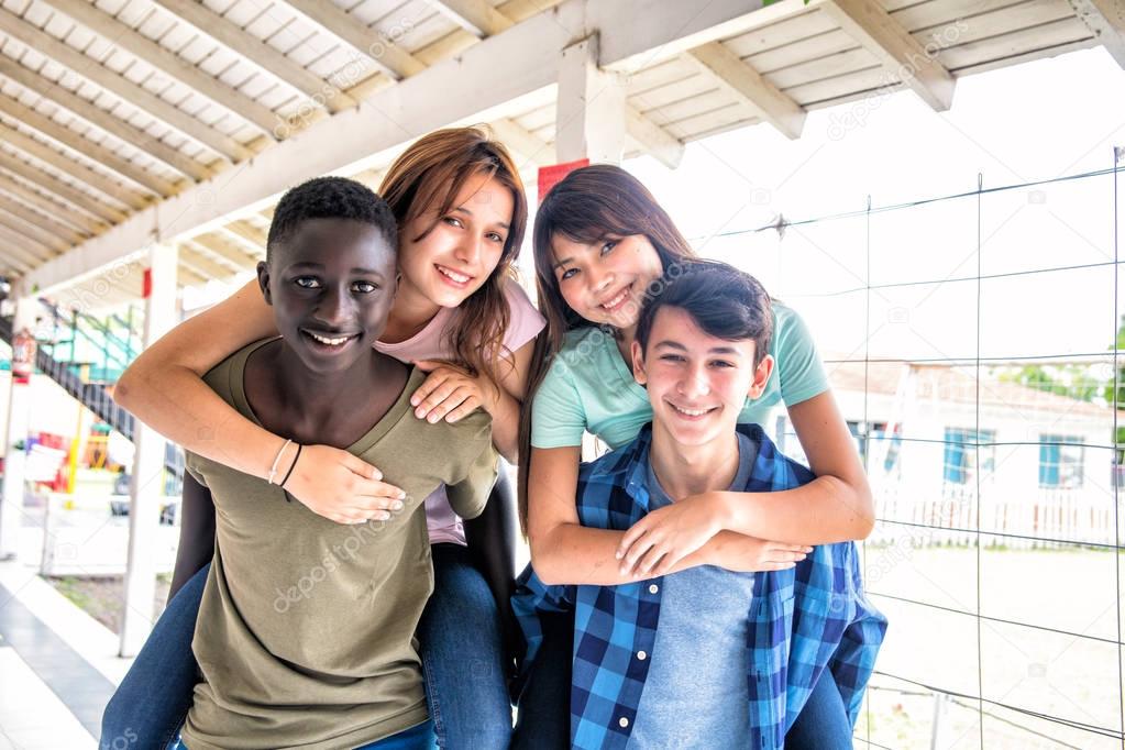 Two couples of mixed races teenagers playing piggyback at achool