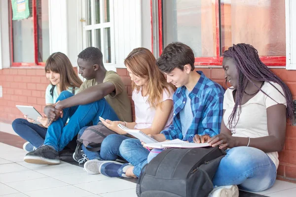 Grupo de adolescentes de raza mixta leyendo libros y tabletas en la escuela — Foto de Stock