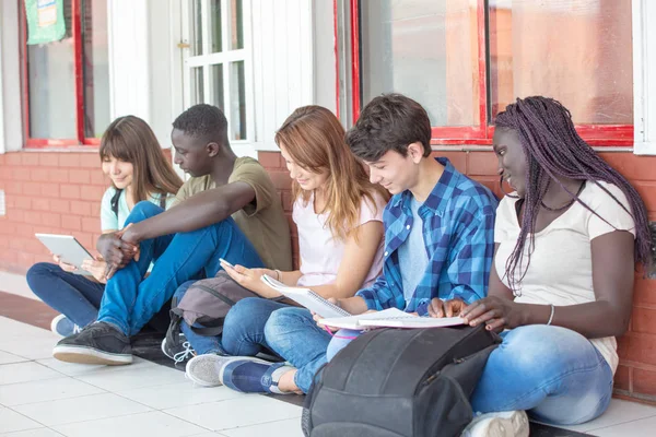 Grupo de adolescentes de raza mixta leyendo libros y tabletas en la escuela —  Fotos de Stock