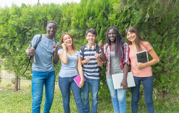 Группа мультиэтнических подростков отдыхает в парке улыбаясь остроумие — стоковое фото