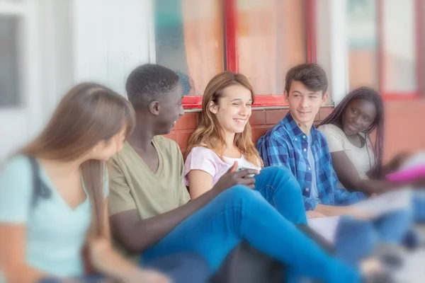 Grupo de adolescentes sonriendo sentados en el pasillo de entrada de la escuela — Foto de Stock